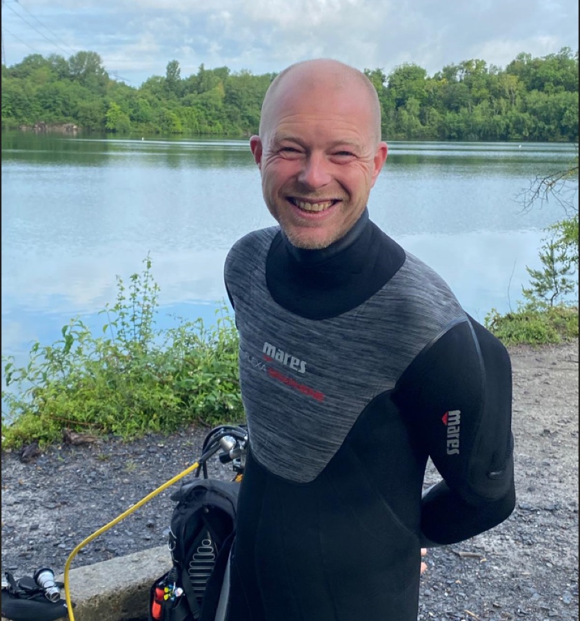 Membre du club en combinaison, souriant au bord de l'eau avant une plongée