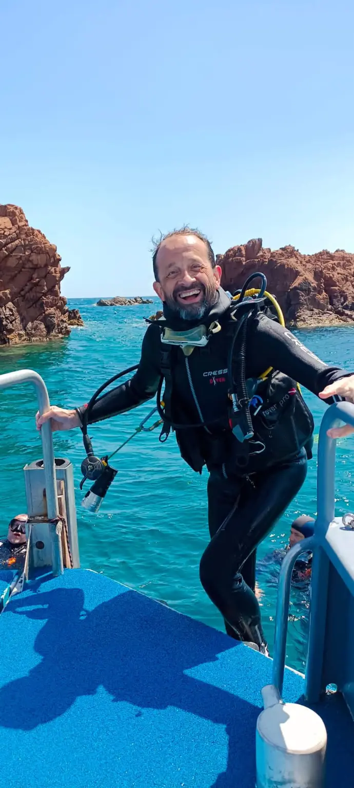Plongeur du club remontant sur le bateau, tout sourire, devant les roches rouges